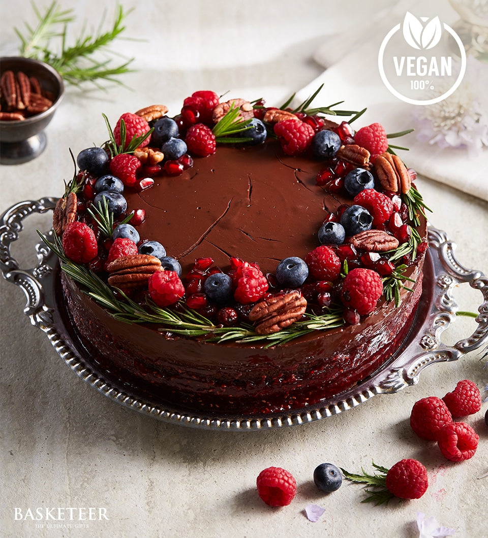 Dark chocolate vegan cake topped with fresh raspberries, blueberries, and pecans on silver platter