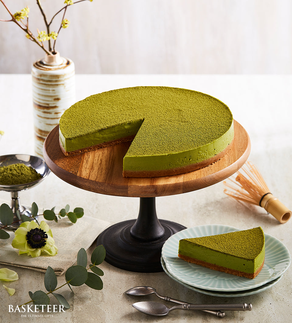 Vibrant matcha cheesecake with creamy green filling and brown crust, plated on light blue ceramic with matcha powder garnish