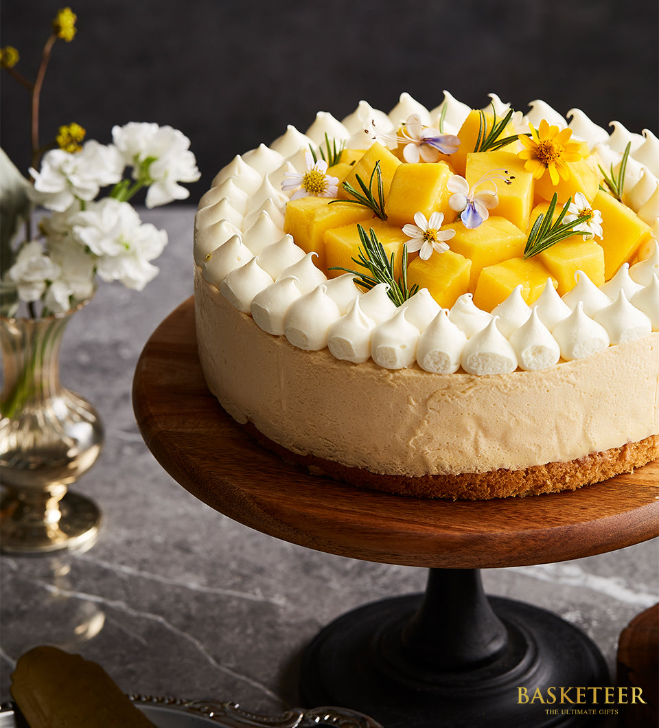 Vanilla mango mousse cake with meringue border, fresh diced mango, edible flowers, and rosemary on wooden stand