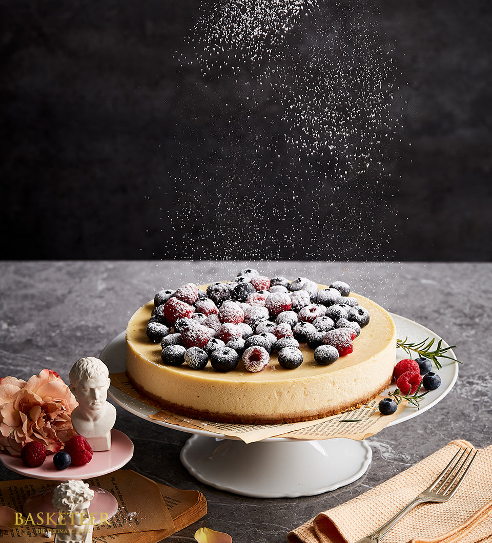 Mixed berry cheesecake with raspberries and blueberries on white cake stand, dusted with powdered sugar