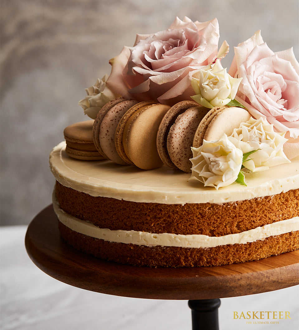 Vanilla butter cake with white frosting, pink roses, and macarons on wooden stand for birthday celebrations