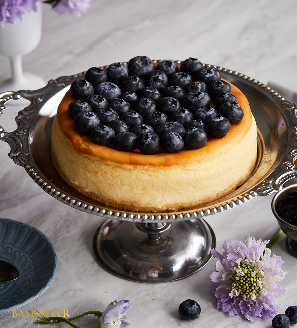 Blueberry New York cheesecake with golden crust on ornate silver stand, birthday celebration cake