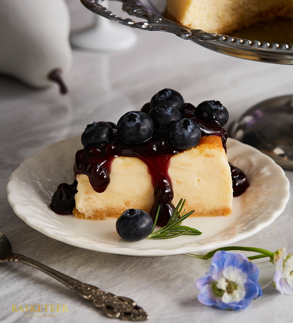 Creamy New York cheesecake slice topped with blueberry compote and fresh blueberries on white scalloped plate