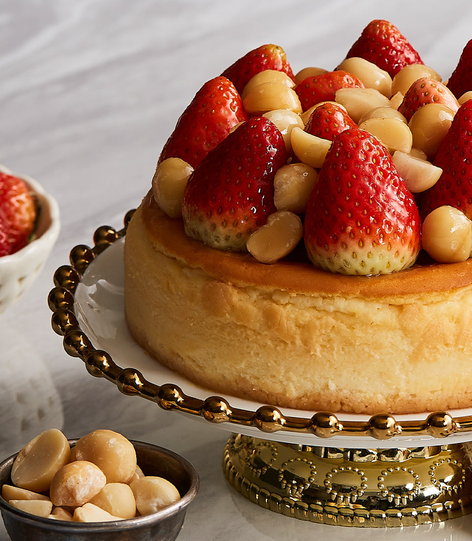 Strawberry macadamia cheesecake with fresh berries and nuts on gold-rimmed cake stand