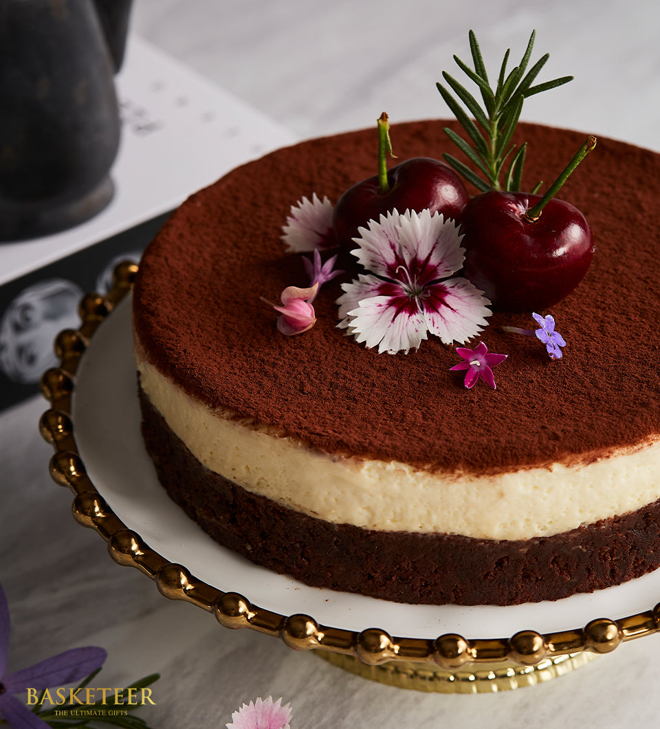 Sinfully Rich two-layer chocolate cake with cocoa powder, cherries, and fresh flowers on gold stand