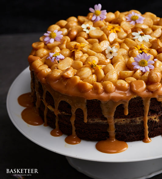 Layered chocolate cake with macadamia caramel topping and edible flowers on white stand