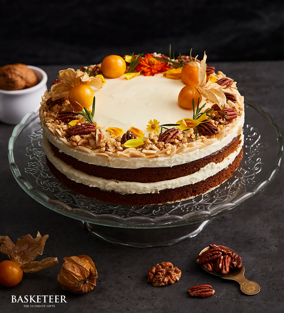 Three-layer carrot cake with cream cheese frosting, pecans, walnuts, and fresh physalis on glass stand