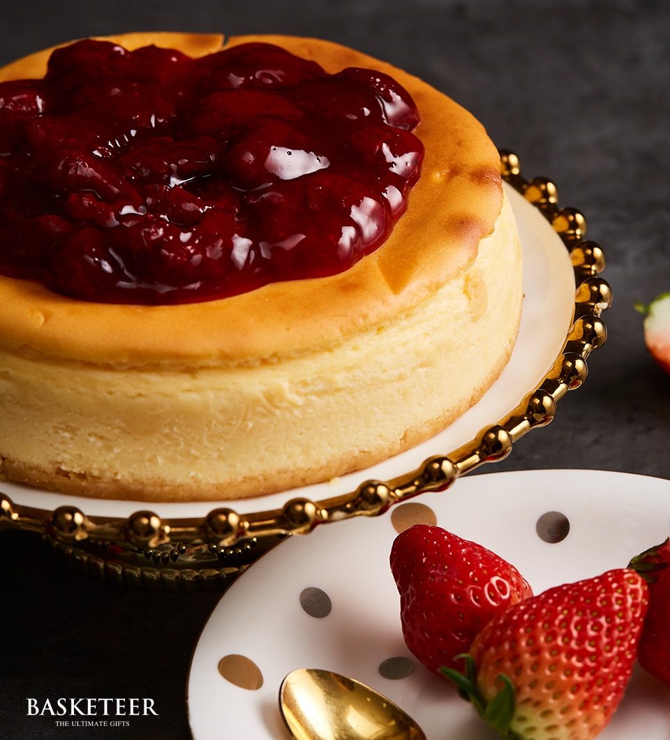 Golden cheesecake with dark red strawberry jam topping on ornate gold stand, fresh strawberries and polka dot plate