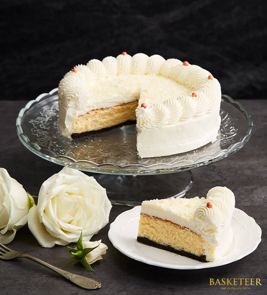 White chocolate cheesecake with dark crust and piped cream swirls, presented on glass cake stand with roses for birthday