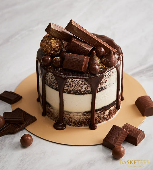 Semi-naked chocolate layer cake with chocolate ganache drip, topped with Hershey's bars, Kit Kat, and gold-dusted truffles