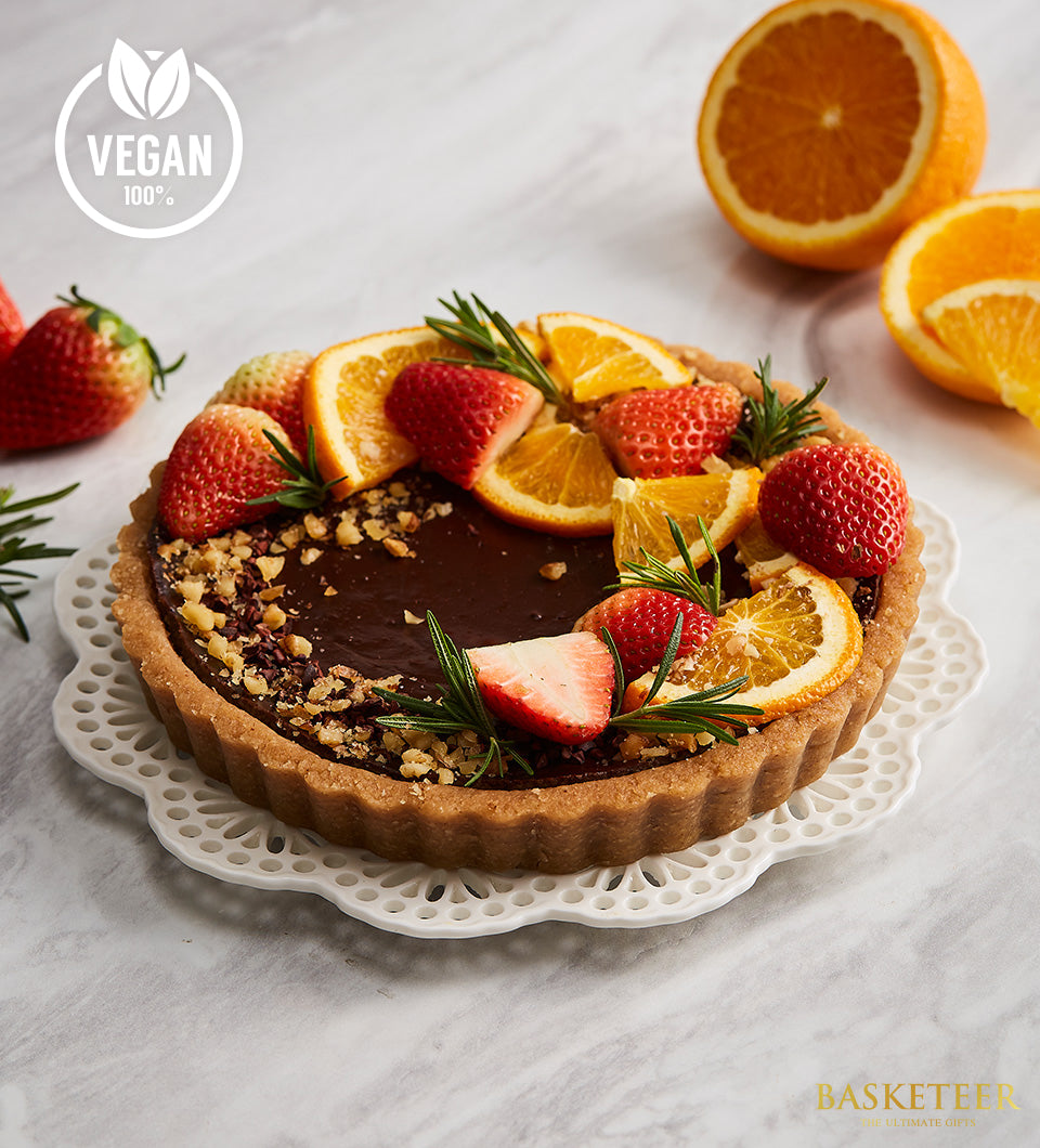Dark chocolate vegan tart with fresh strawberries, orange, and rosemary on artisan ceramic plate