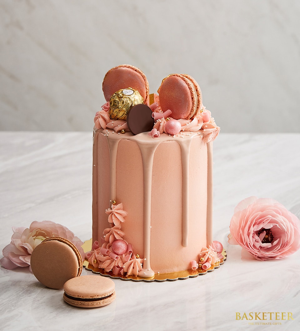 Tall peach layer cake with chocolate drip, macarons, and gold sprinkles for birthdays