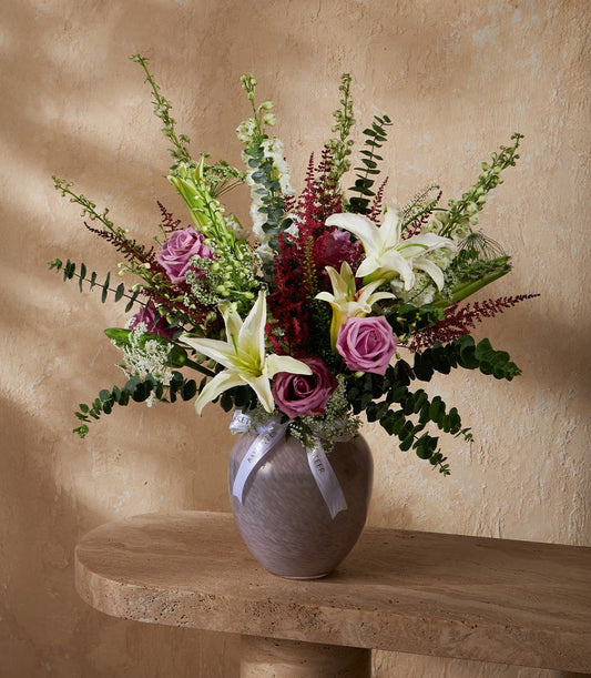 Fresh white lilies and deep pink roses with green foliage in mottled grey-purple glass vase