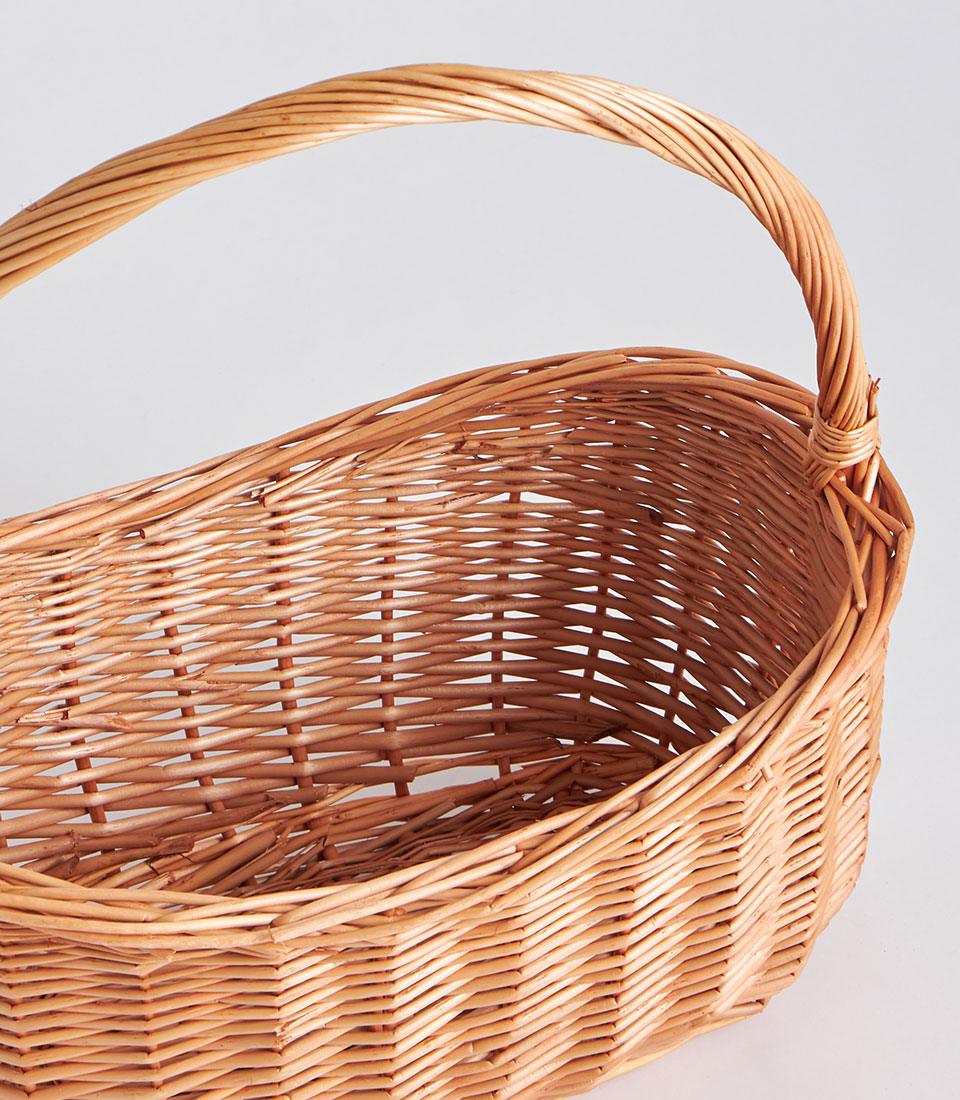 Handwoven light brown oval wicker basket with tall arched handle, natural willow weave