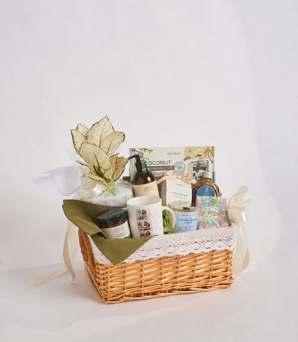 Wicker basket gift set with cream linen, botanical products, dried flowers, coconut rejuvenation kit, cream ribbon handles on white background.