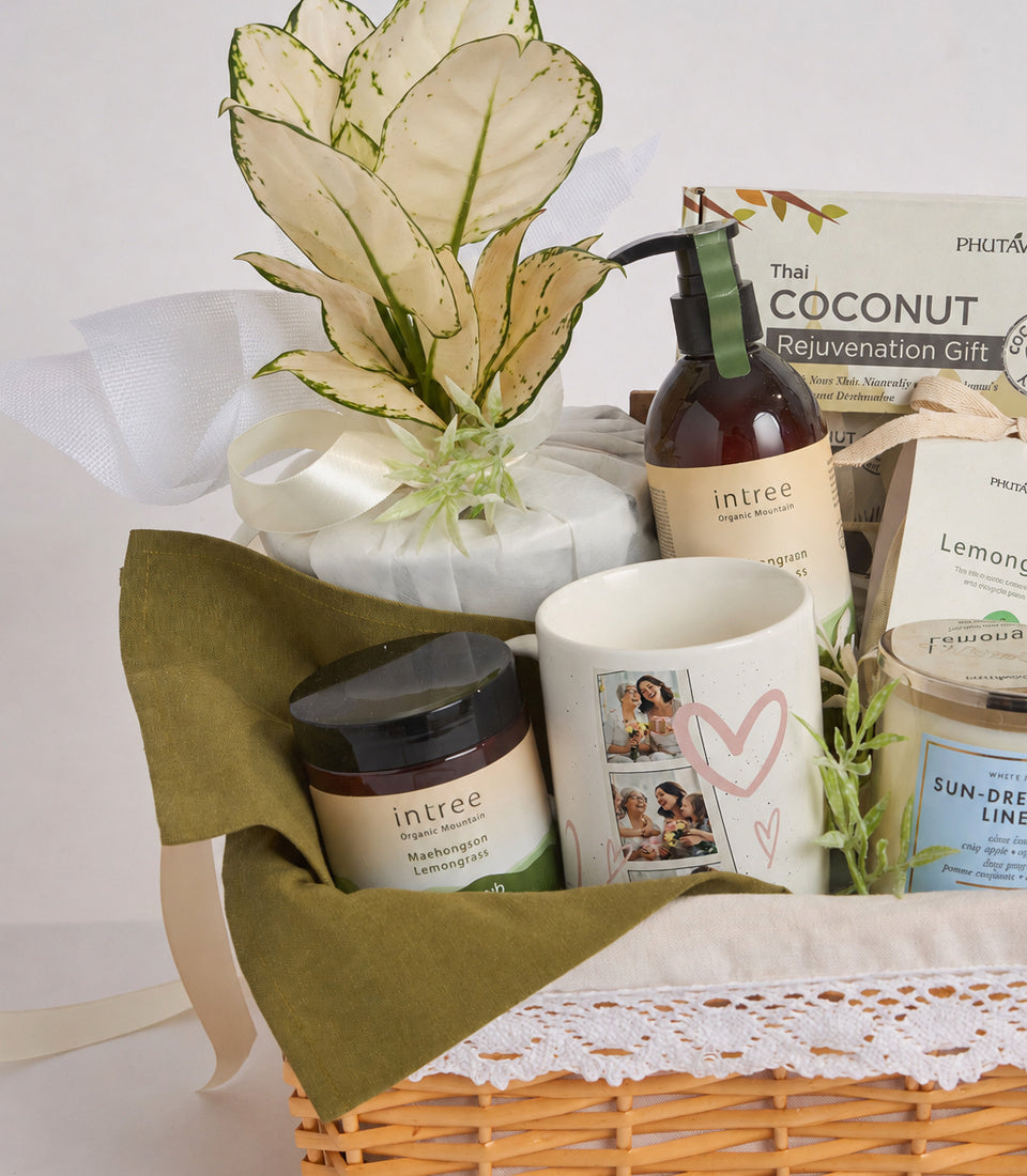Curated gift basket with green fabric bow, wicker base, dried flowers, intree organic products, personalized mug with photos and hearts, and Thai coconut rejuvenation items.