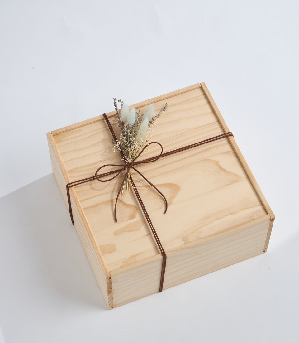 Wooden gift box with natural pine finish, tied with brown twine bow and dried flowers decoration on white background.