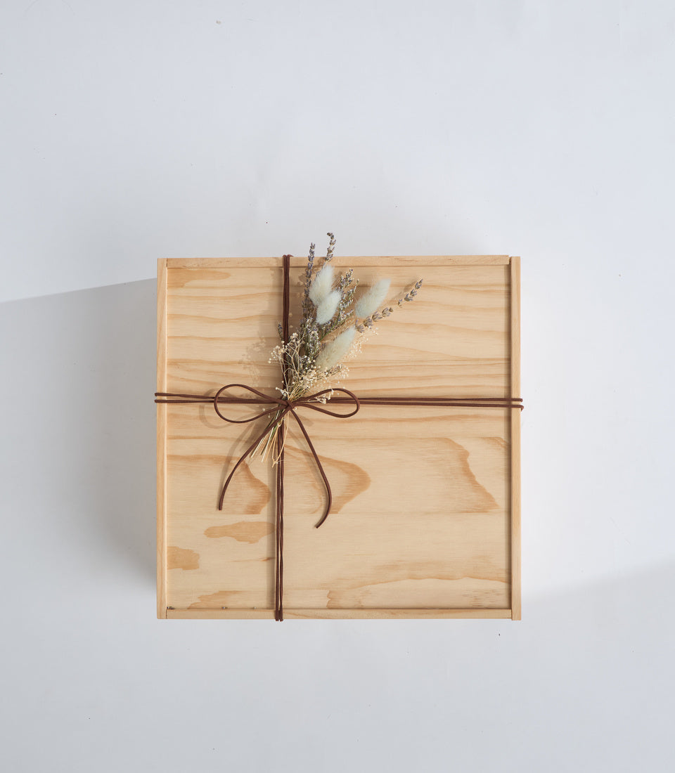 Wooden gift box with brown ribbon bow and dried flower arrangement on white background, minimalist aesthetic.