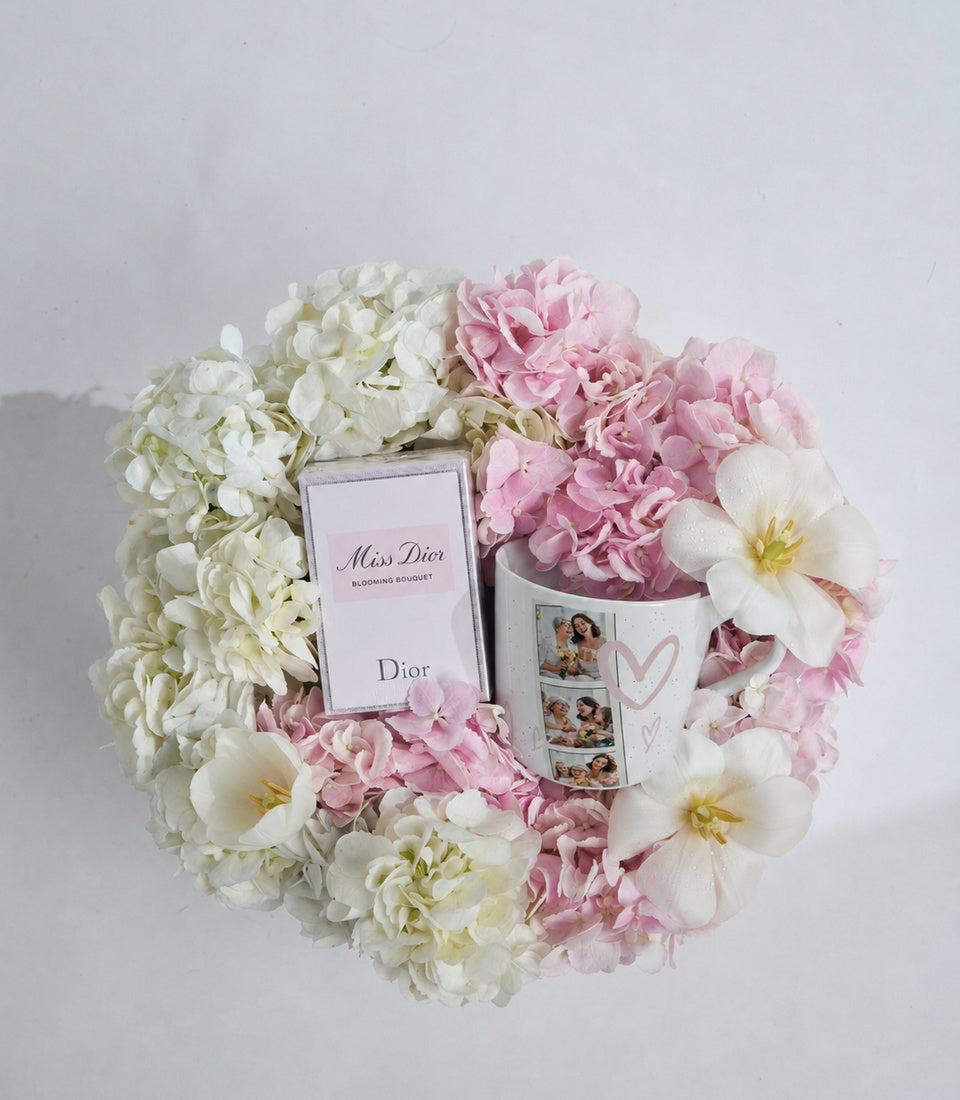 Luxury flower arrangement with Miss Dior perfume box, pink and white hydrangeas, peonies, and photo cards on white background.