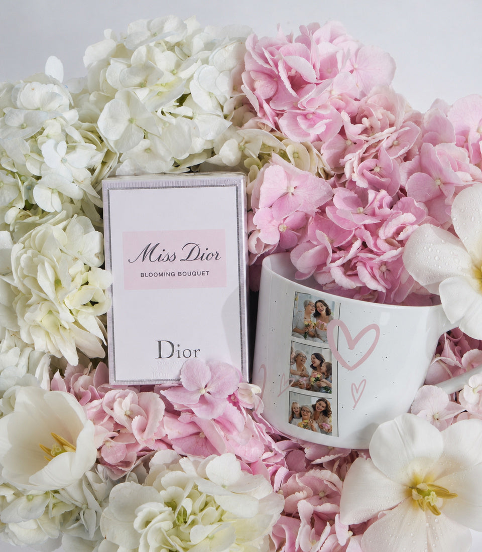 Miss Dior Blooming Bouquet fragrance box surrounded by pink and white hydrangeas and peonies, with personalized photo mug featuring pink hearts.