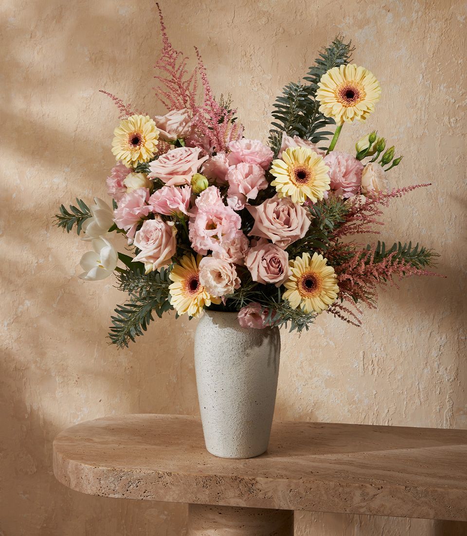 Pastel pink and yellow flowers in grey ceramic vase with roses, gerberas, and feathery astilbe