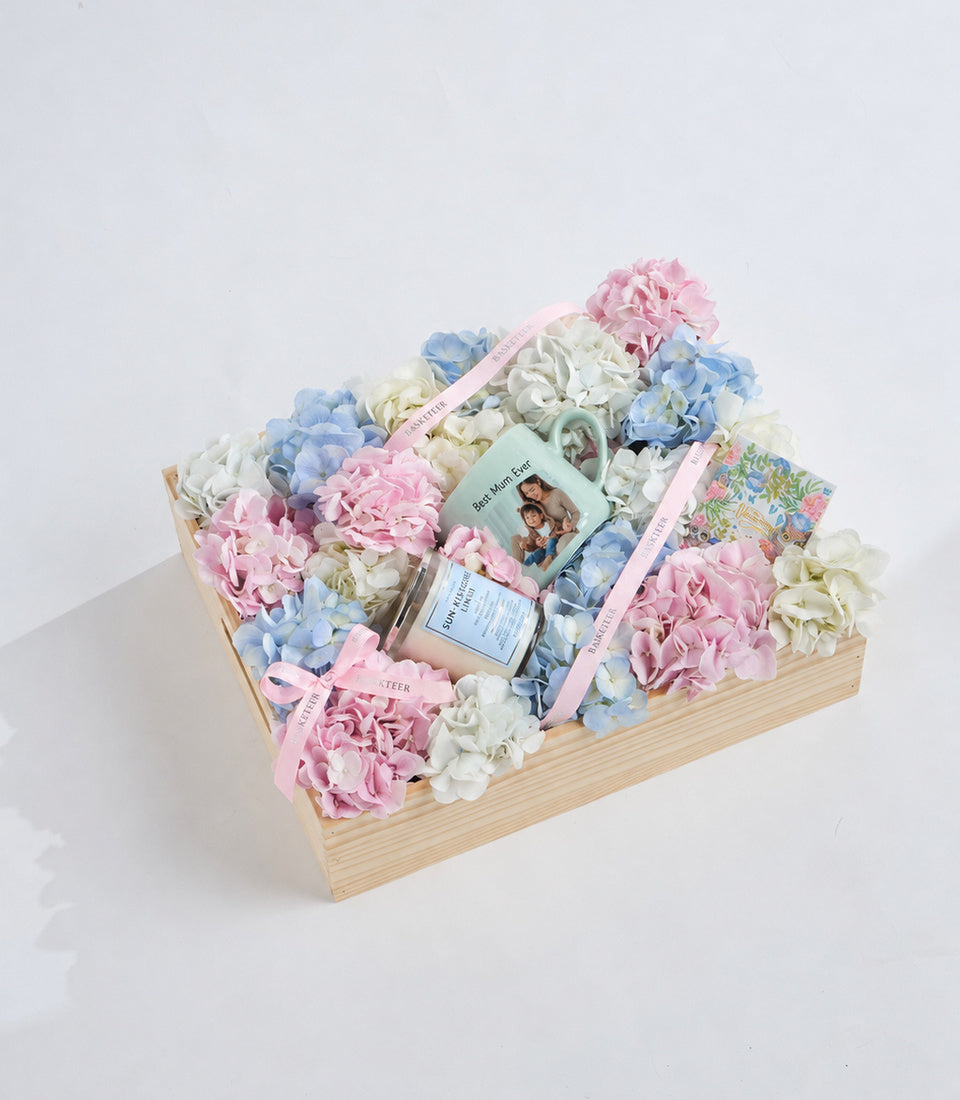 Luxury floral gift box with pink, blue, and white hydrangeas in natural wood container with skincare products and ribbons.