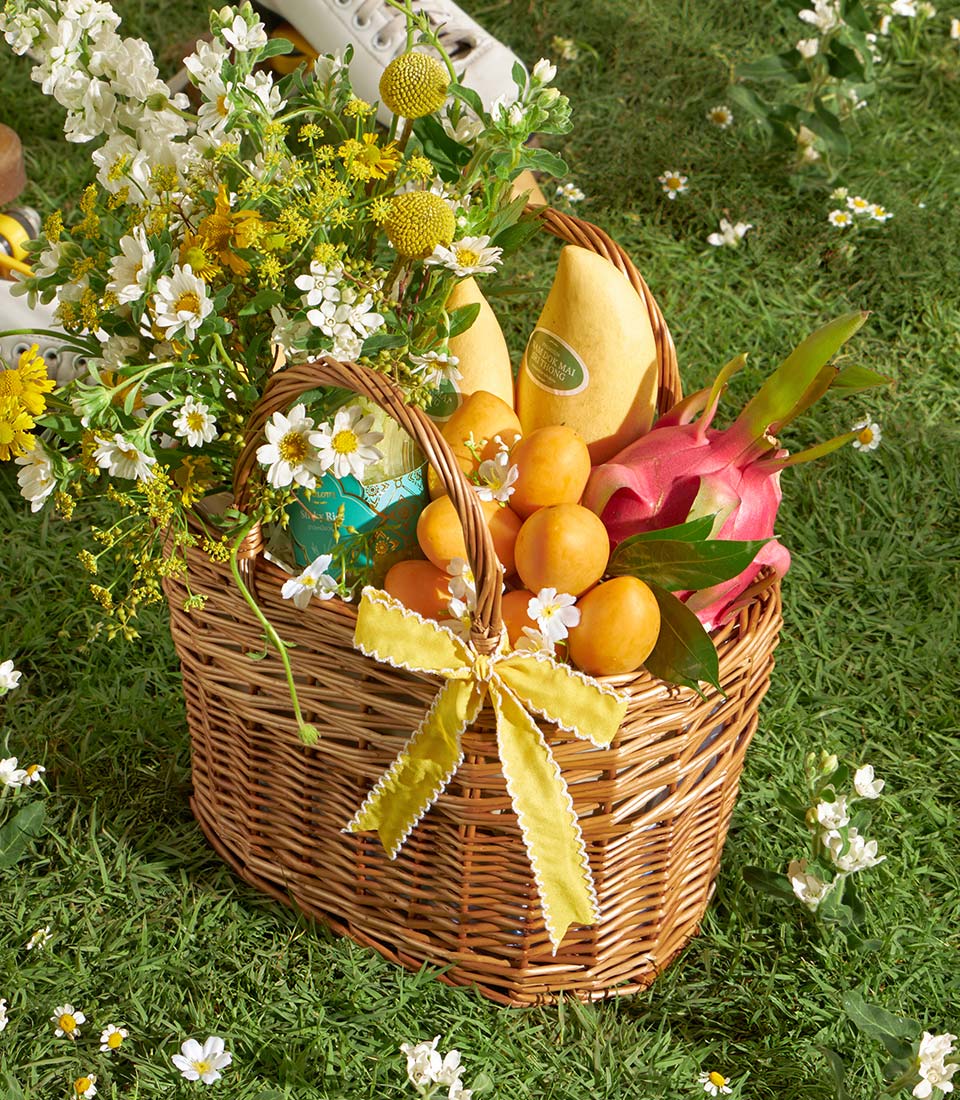 Luxury wicker gift basket with tropical mangoes, fresh flowers, and dragon fruit on green lawn
