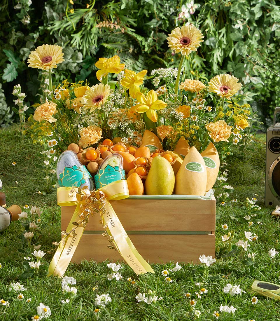 Tropical fruit crate with yellow mangoes, pears, and physalis in wooden basket with gold-ribbon bow