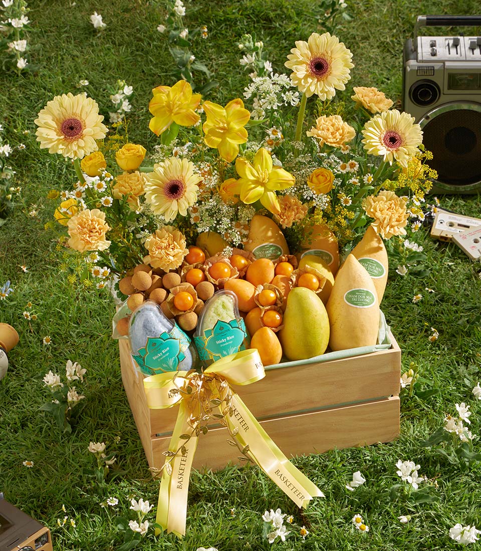 Sunny Bloom tropical fruit crate with golden mangoes, physalis, and sticky rice, topped with yellow and orange gerbera