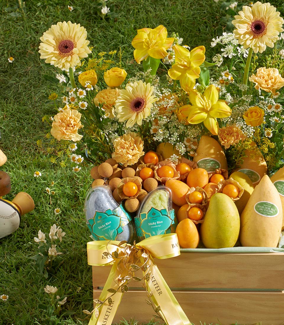 Vibrant tropical fruit crate with Nam Doc Mai mangoes, physalis, and longan in woven basket with sticky rice containers