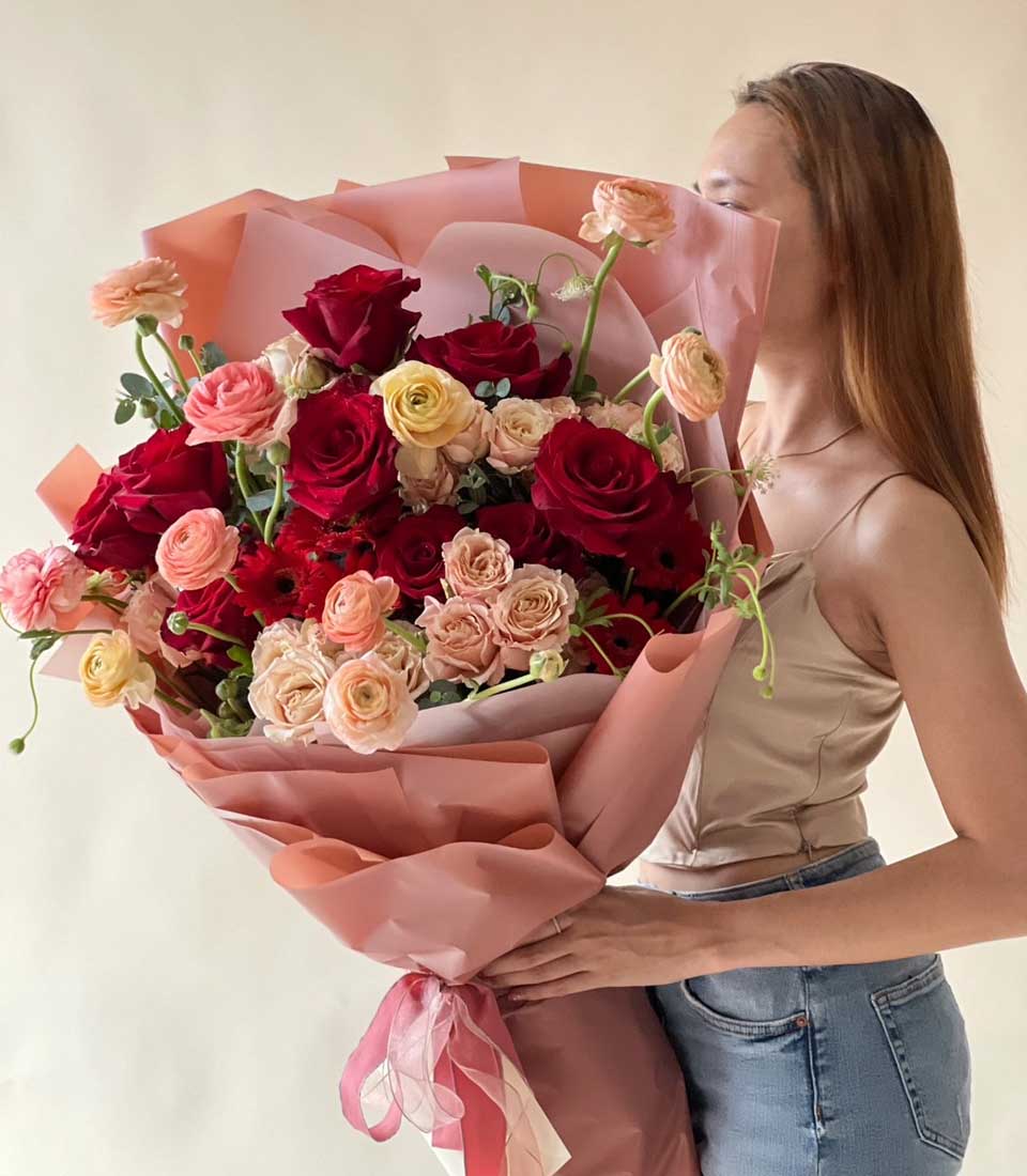Passionate Crimson Rose Bouquet with soft pink wrapping and layered ribbon, featuring red roses and peachy ranunculus