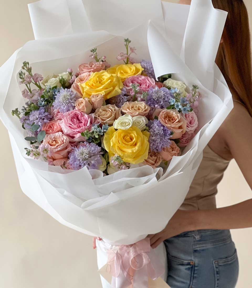 Elegant pastel rose bouquet with yellow, pink, peach, and white roses tied with pink ribbon