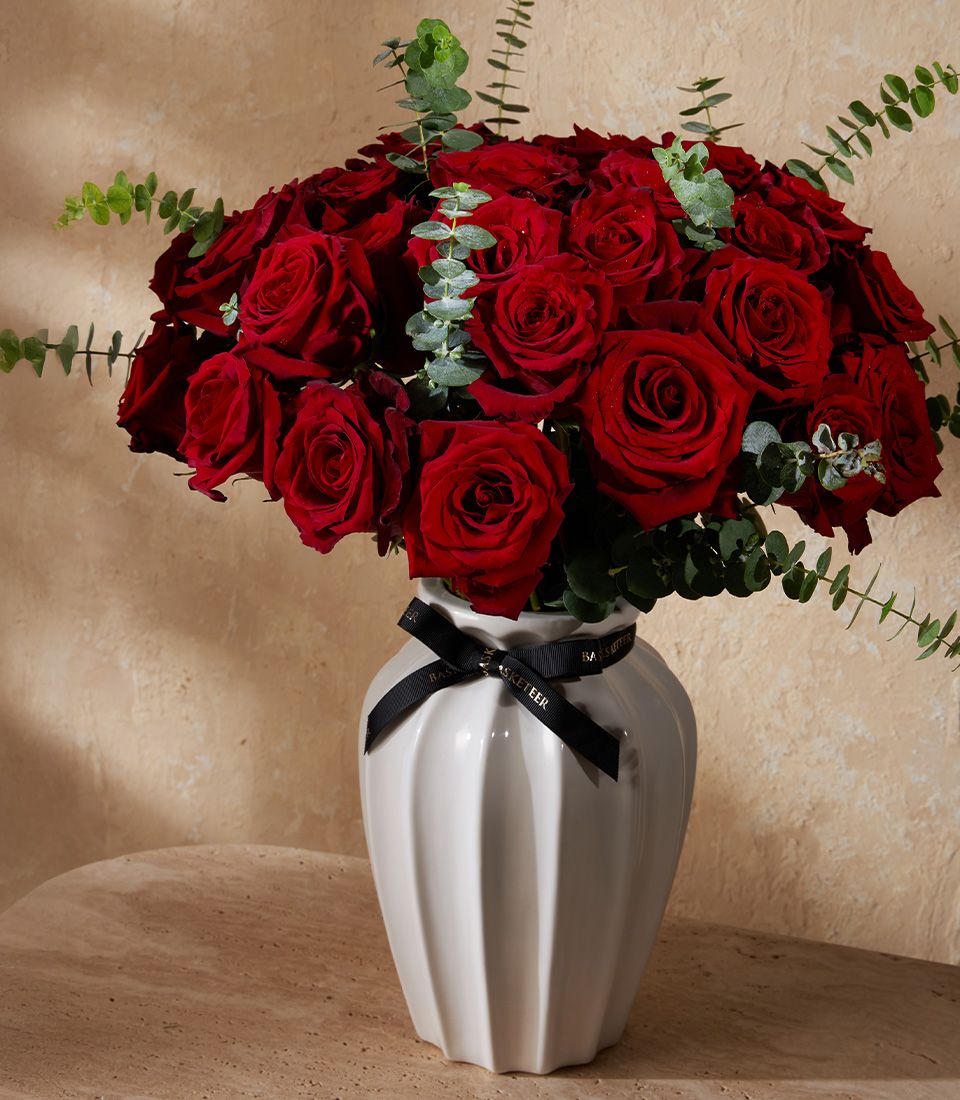 Vibrant scarlet roses and eucalyptus in white ribbed ceramic vase with black bow