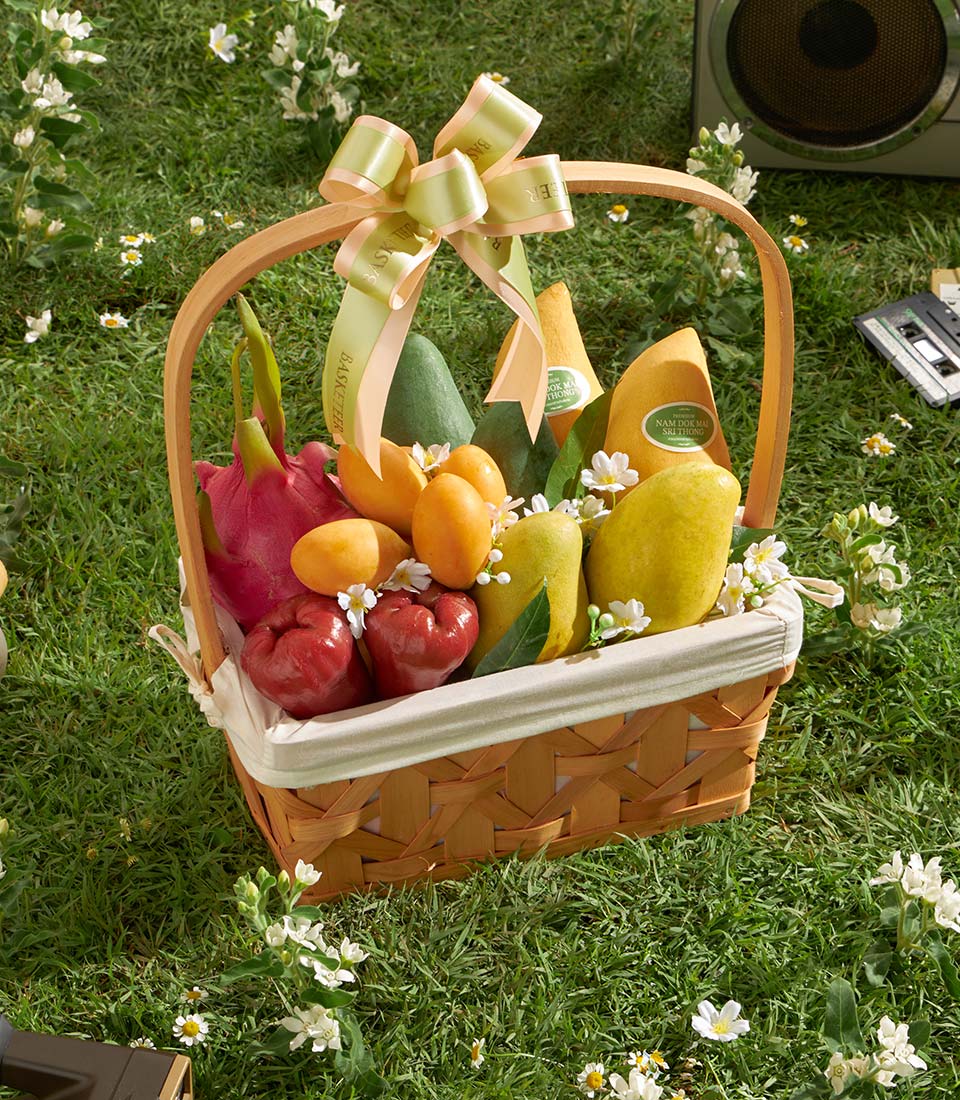 Woven tropical fruit basket with dragon fruit, mangoes, and rose apples on cream linen