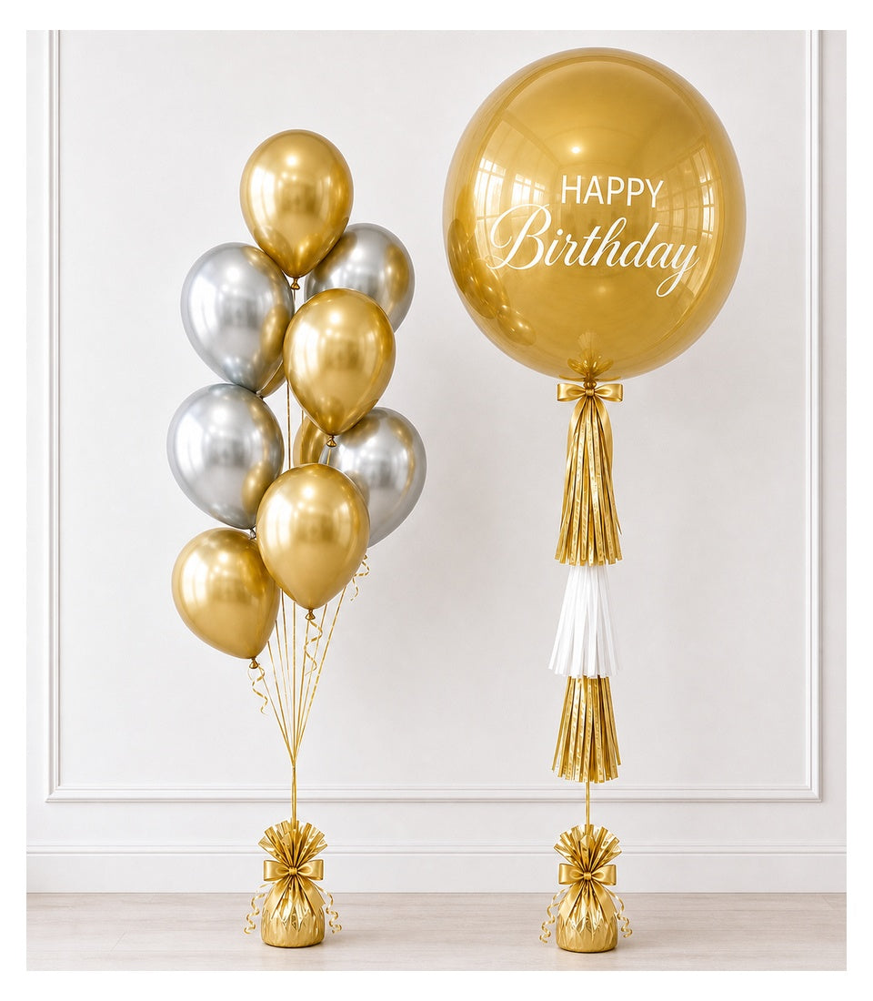 Gold and silver metallic balloons with tassels and gold weights. Large helium balloon reads "HAPPY Birthday" in elegant script font.