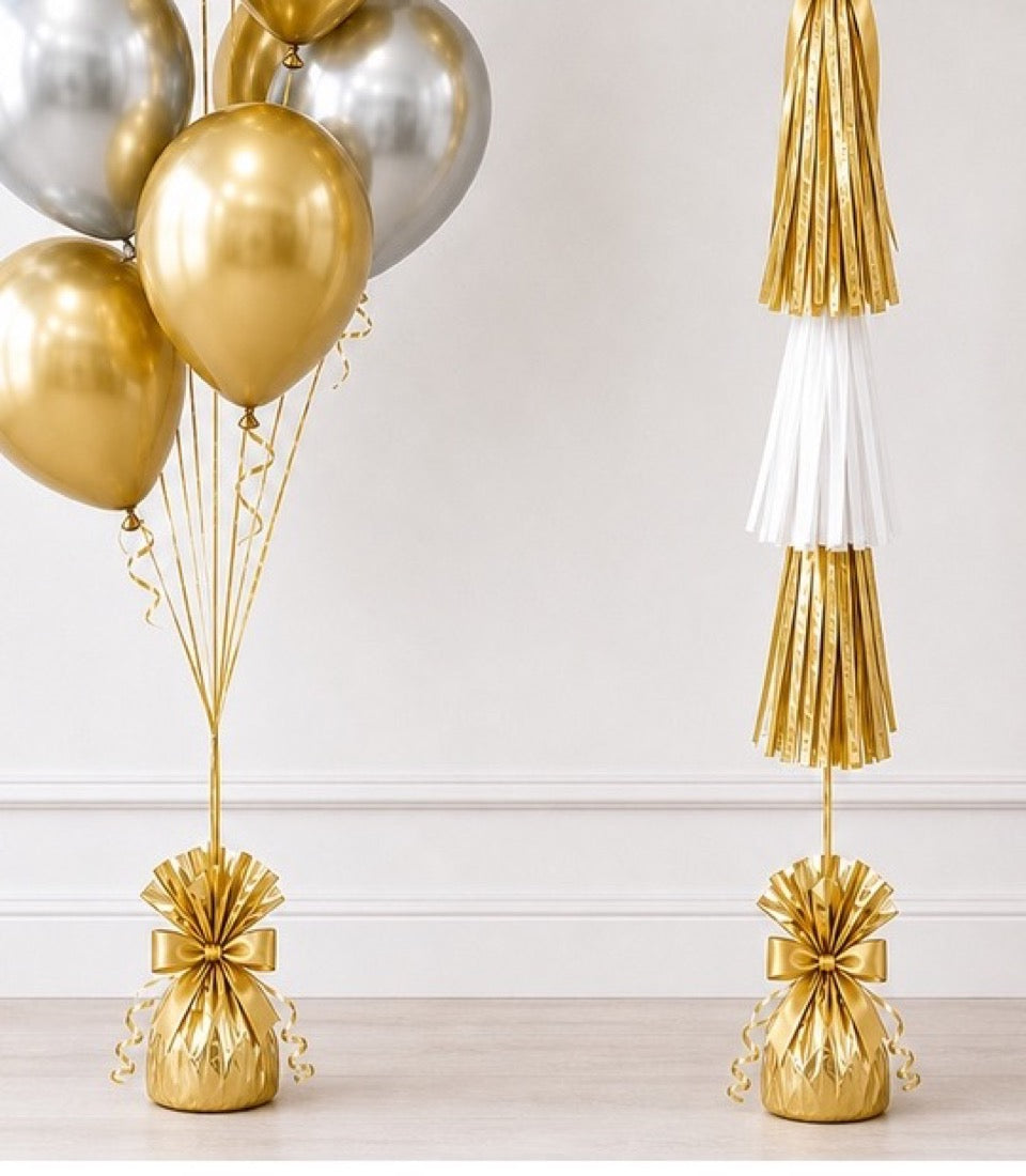 Gold and silver balloons with tassel garlands and gold gift bag weights in elegant celebration decor setup.