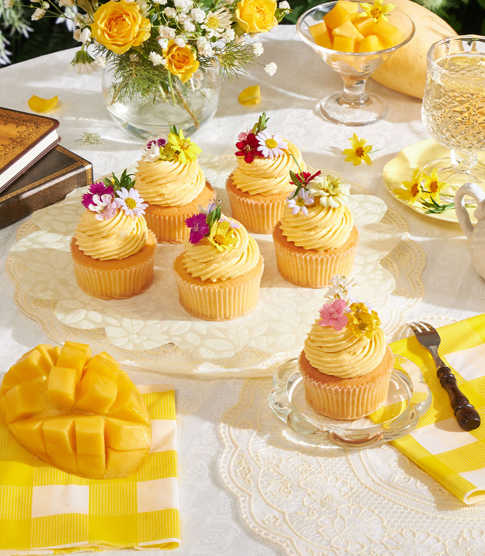 Golden mango buttercream cupcakes with fresh flower toppers and mango jam filling on white cake stand