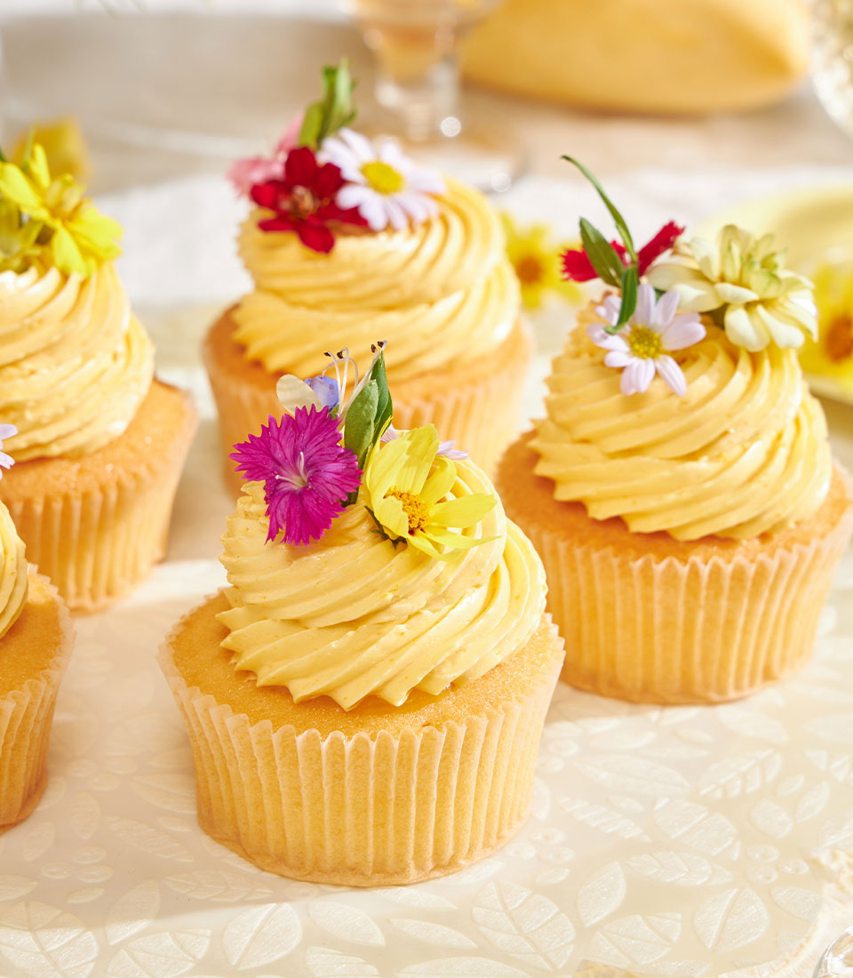 Golden mango buttercream cupcakes with fresh flower garnish, mango jam filled sponge cake