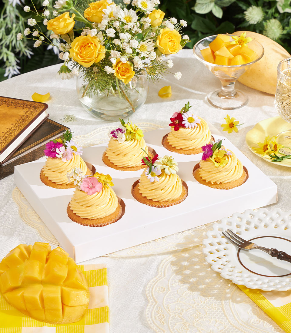 Golden mango buttercream cupcakes with fresh flower toppers and yellow roses in garden setting