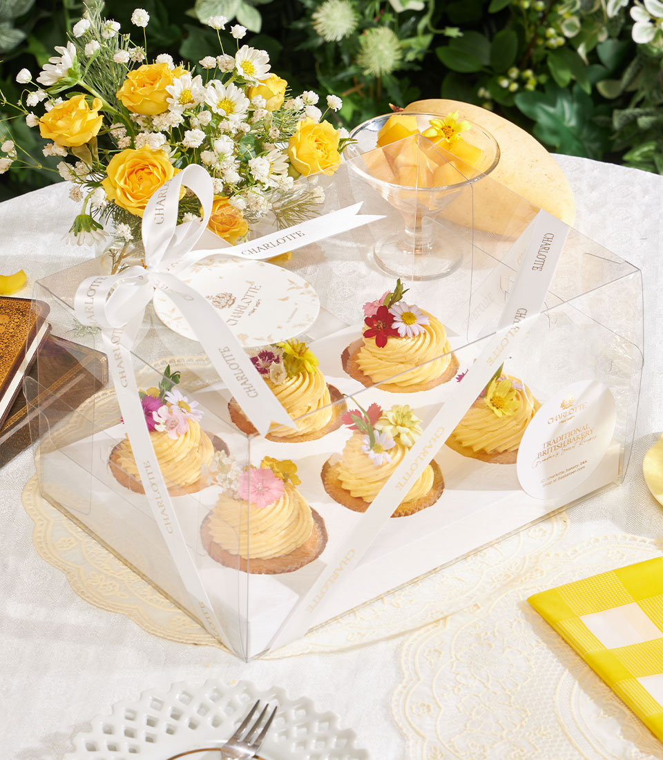 Golden mango buttercream cupcakes with edible flowers in Charlotte Bakery gift box with yellow roses