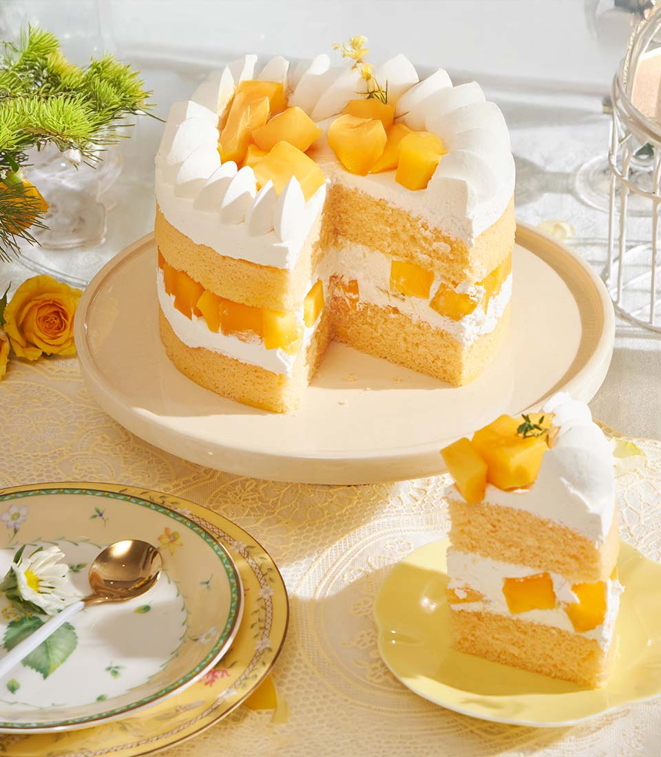 Golden mango chiffon cake with fresh mango layers and whipped cream on elegant cake stand
