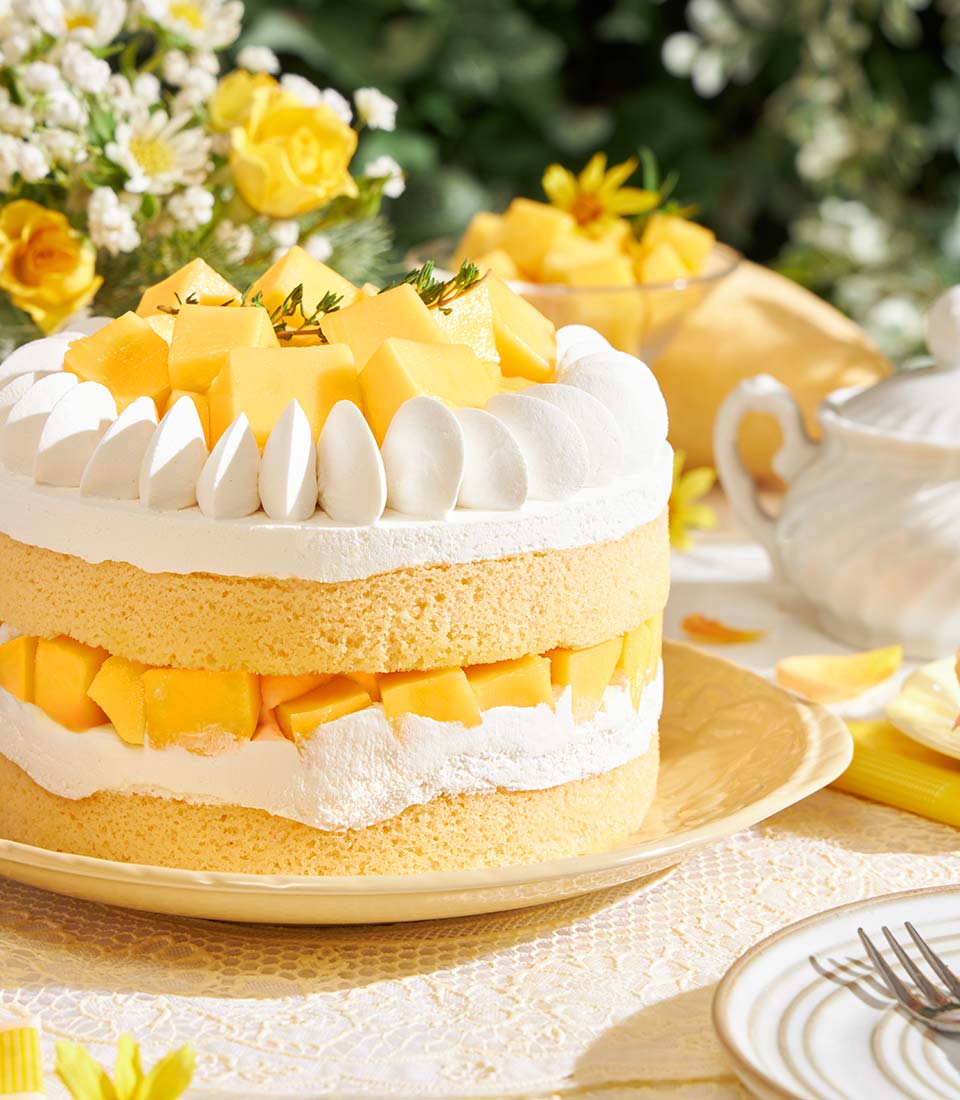 Golden mango layer cake with fresh mango chunks and whipped cream frosting on ceramic plate