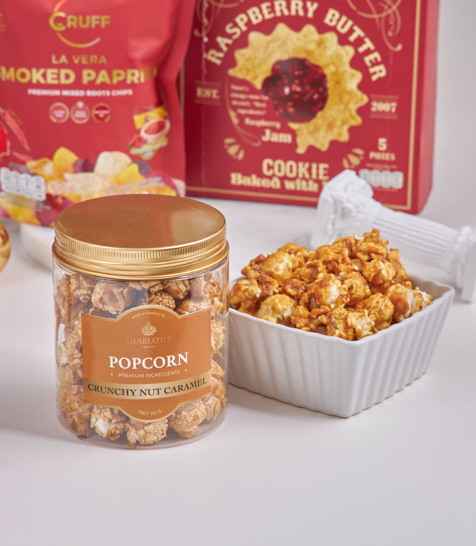 Luxury gourmet New Year gift basket with caramel popcorn, paprika chips, and raspberry butter cookies on white table