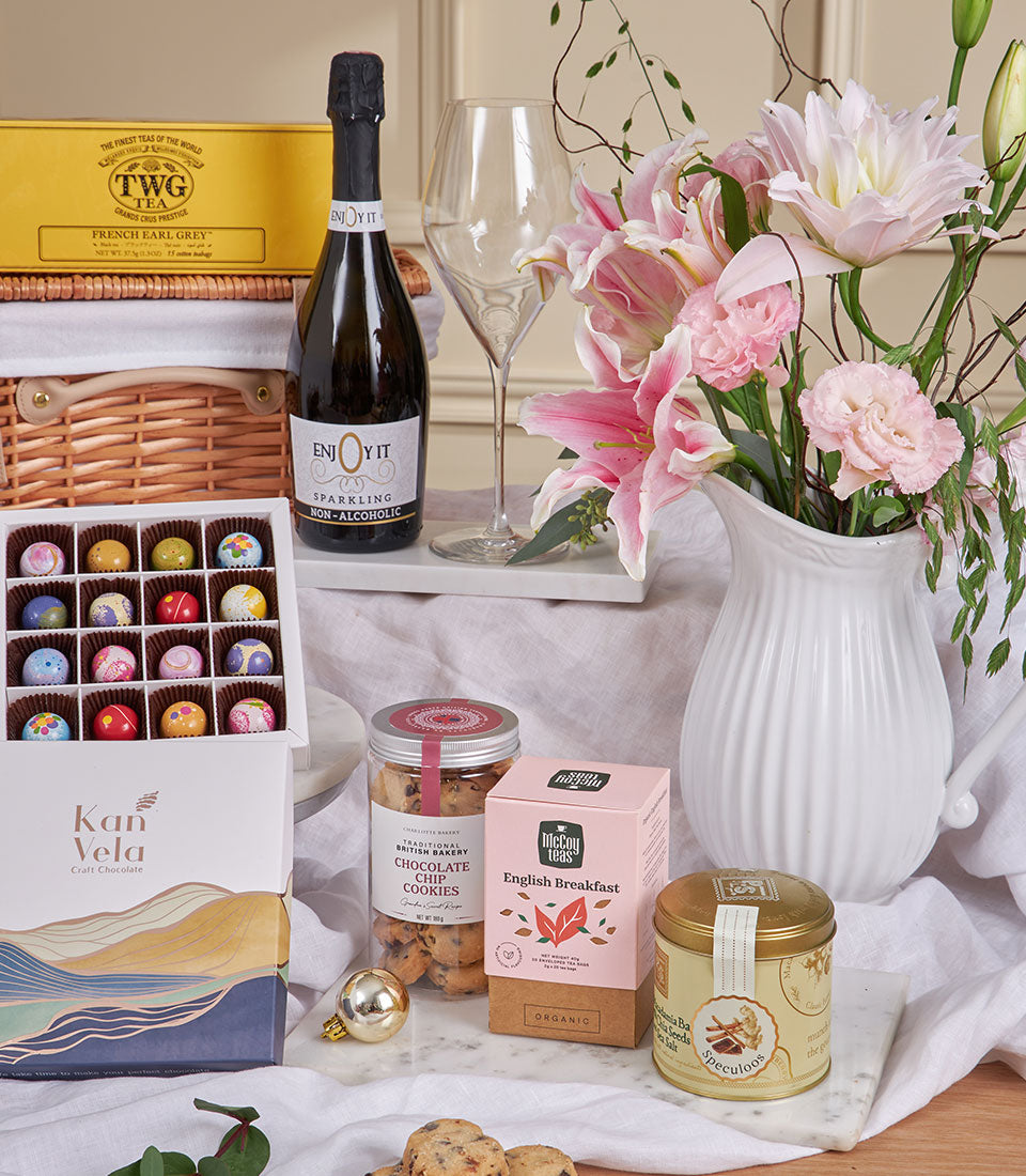 Champagne-style luxury chocolate celebration box with gourmet tea, cookies, and pink lily flowers for New Year gifting
