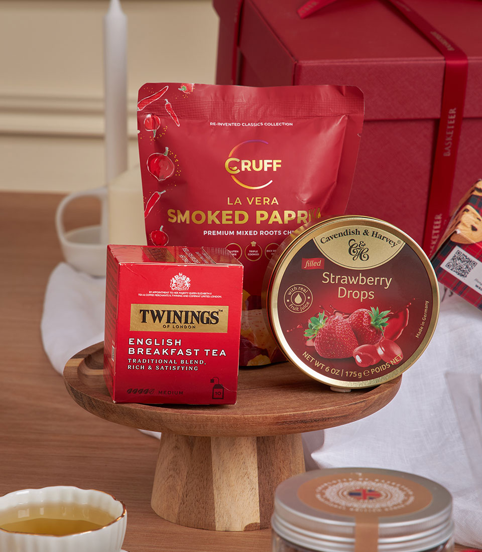 Red velvet gourmet gift basket with English breakfast tea, smoked paprika, and strawberry drops on wooden stand