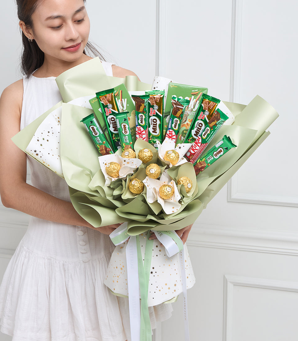 Woman in white dress holding green wrapped bouquet with gold chocolate candies and assorted snack packets arranged as flowers.
