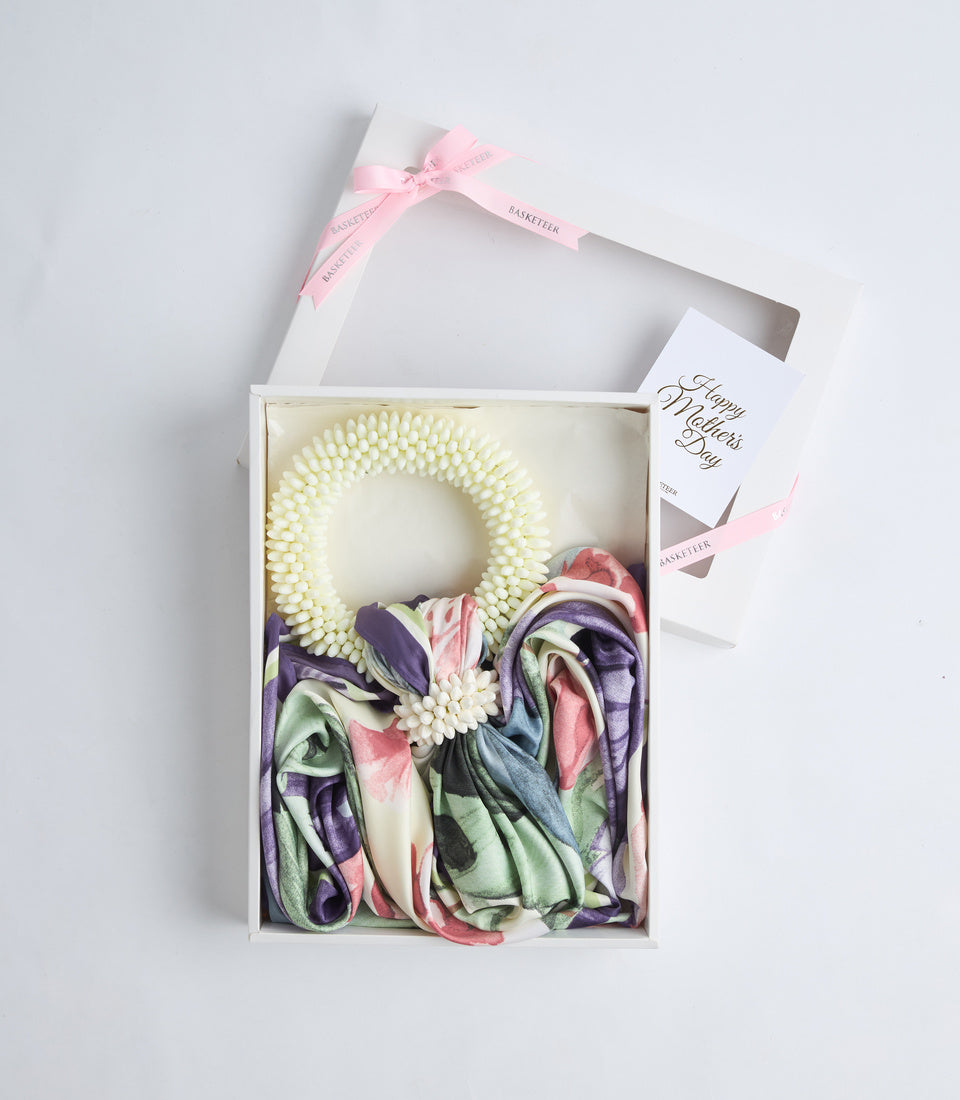 White gift box containing cream pearl beaded wreath, colorful floral scarf, and Happy Mother's Day card with pink ribbon handles.