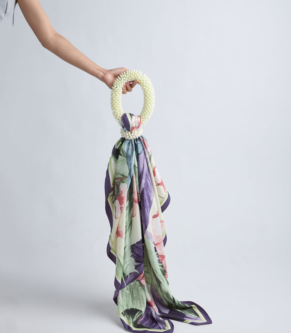 Cream pearl beaded bracelet scarf holder with floral patterned fabric in purple, green, pink, and cream tones draped below.