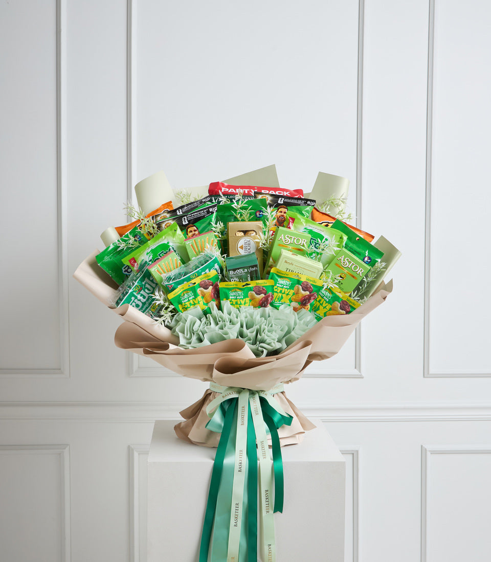 # Alt Text

Vibrant snack bouquet with green and yellow packaged foods arranged in kraft paper wrapping, tied with green ribbons, featuring crinkled mint filler and red accent bow.
