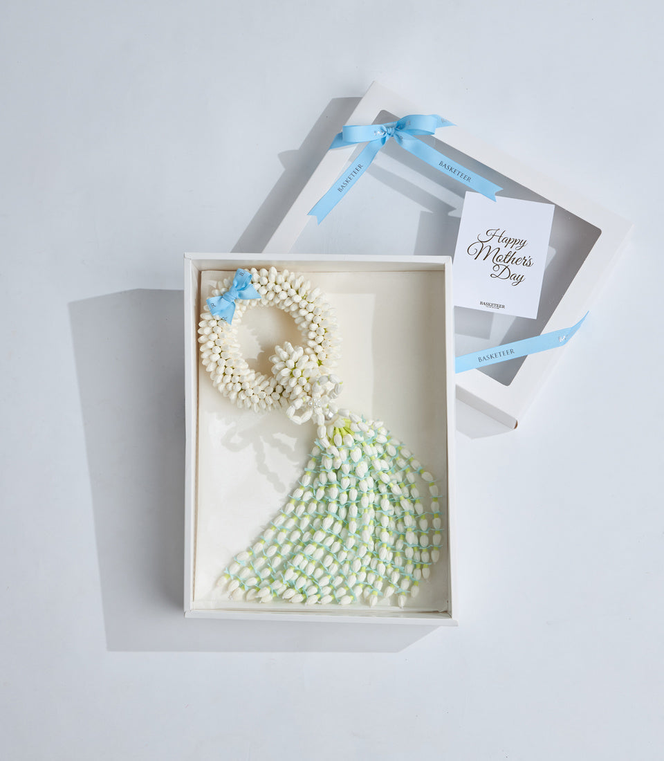 Elegant Mother's Day gift box with white flowers arranged in a dress silhouette, blue ribbon bow, and greeting card from Basketeer.